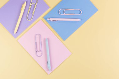 Sarı arka planda pembe, mor ve mavi defterlerin üst görüntüsü. Pembe, sarı ve mavi kalemler, ataçlar, okul, ofis kağıdı. Düz yat, boşluğu kopyala.