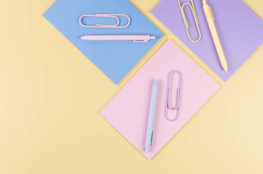 Sarı arka planda pembe, mor ve mavi defterlerin üst görüntüsü. Pembe, sarı ve mavi kalemler, ataçlar, okul, ofis kağıdı. Düz yat, boşluğu kopyala.