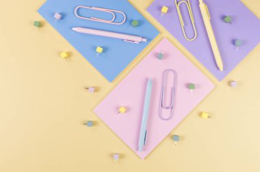 Sarı arka planda pembe, mor ve mavi defterlerin üst görüntüsü. Renkli kalemler, ataçlar, raptiyeler, okul, ofis kağıdı. Düz yat, boşluğu kopyala.