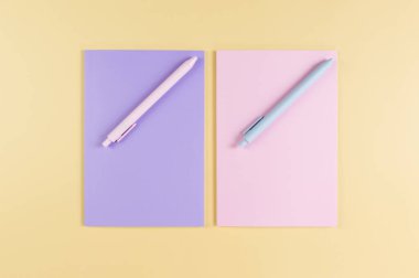 Pembe ve mor defterlerin üst görüntüsü, sarı arka planda pembe ve mavi kalemler. Okul, ofis duvar kağıdı. Düz yat, boşluğu kopyala.