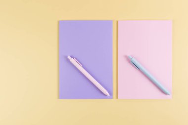 Pembe ve mor defterlerin üst görüntüsü, sarı arka planda pembe ve mavi kalemler. Okul, ofis duvar kağıdı. Düz yat, boşluğu kopyala.