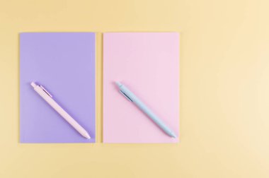 Pembe ve mor defterlerin üst görüntüsü, sarı arka planda pembe ve mavi kalemler. Okul, ofis duvar kağıdı. Düz yat, boşluğu kopyala.