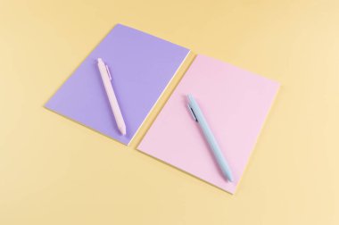Pembe ve mor defterlerin üst görüntüsü, sarı arka planda pembe ve mavi kalemler. Okul, ofis duvar kağıdı. Düz yat, boşluğu kopyala.