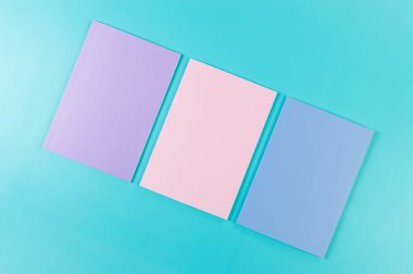 Mavi arka planda pembe, mor ve mavi defterlerin üst görüntüsü. Okul, ofis duvar kağıdı. Düz yat, boşluğu kopyala.