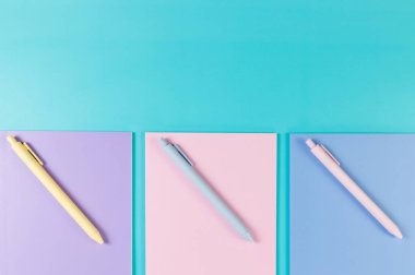 Mavi arka planda pembe, mor ve mavi defterlerin üst görüntüsü. Pembe, sarı ve mavi kalemler, okul, ofis kağıdı. Düz yat, boşluğu kopyala.