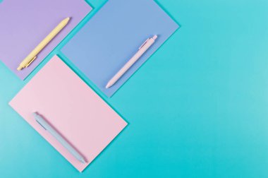 Mavi arka planda pembe, mor ve mavi defterlerin üst görüntüsü. Pembe, sarı ve mavi kalemler, okul, ofis kağıdı. Düz yat, boşluğu kopyala.