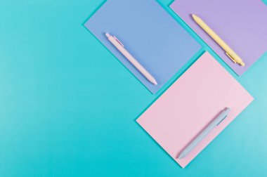 Mavi arka planda pembe, mor ve mavi defterlerin üst görüntüsü. Pembe, sarı ve mavi kalemler, okul, ofis kağıdı. Düz yat, boşluğu kopyala.