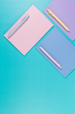 Mavi arka planda pembe, mor ve mavi defterlerin üst görüntüsü. Pembe, sarı ve mavi kalemler, okul, ofis kağıdı. Düz yat, boşluğu kopyala.