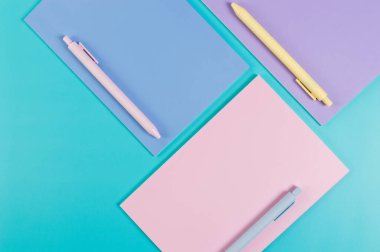 Mavi arka planda pembe, mor ve mavi defterlerin üst görüntüsü. Pembe, sarı ve mavi kalemler, okul, ofis kağıdı. Düz yat, boşluğu kopyala.
