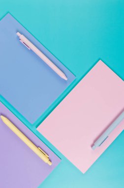 Mavi arka planda pembe, mor ve mavi defterlerin üst görüntüsü. Pembe, sarı ve mavi kalemler, okul, ofis kağıdı. Düz yat, boşluğu kopyala.