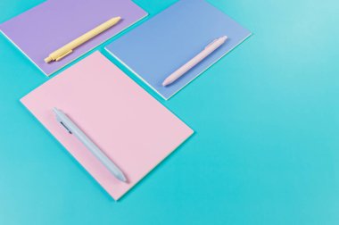 Mavi arka planda pembe, mor ve mavi defterlerin üst görüntüsü. Pembe, sarı ve mavi kalemler, okul, ofis kağıdı. Düz yat, boşluğu kopyala.