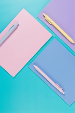 Mavi arka planda pembe, mor ve mavi defterlerin üst görüntüsü. Pembe, sarı ve mavi kalemler, okul, ofis kağıdı. Düz yat, boşluğu kopyala.