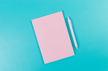 Pembe defterin üst görüntüsü, mavi arka planda pembe kalem. Okul, ofis duvar kağıdı. Düz yat, boşluğu kopyala.