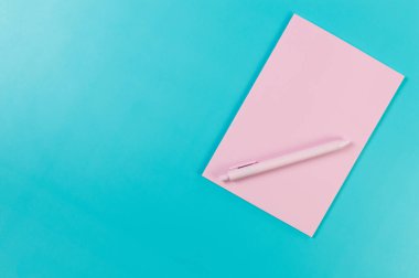 Pembe defterin üst görüntüsü, mavi arka planda pembe kalem. Okul, ofis duvar kağıdı. Düz yat, boşluğu kopyala.