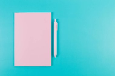 Pembe defterin üst görüntüsü, mavi arka planda pembe kalem. Okul, ofis duvar kağıdı. Düz yat, boşluğu kopyala.