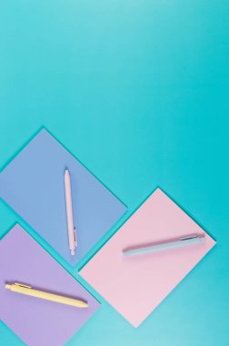 Mavi arka planda pembe, mor ve mavi defterlerin üst görüntüsü. Pembe, sarı ve mavi kalemler, okul, ofis kağıdı. Düz yat, boşluğu kopyala.