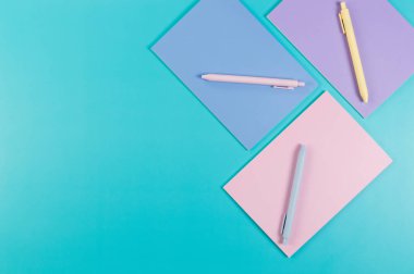 Mavi arka planda pembe, mor ve mavi defterlerin üst görüntüsü. Pembe, sarı ve mavi kalemler, okul, ofis kağıdı. Düz yat, boşluğu kopyala.