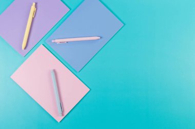 Mavi arka planda pembe, mor ve mavi defterlerin üst görüntüsü. Pembe, sarı ve mavi kalemler, okul, ofis kağıdı. Düz yat, boşluğu kopyala.