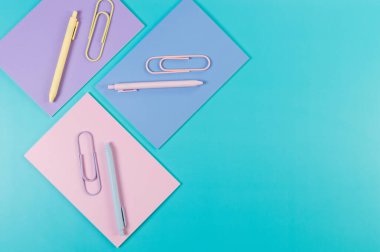 Mavi arka planda pembe, mor ve mavi defterlerin üst görüntüsü. Pembe, sarı ve mavi kalemler, ataçlar, okul, ofis kağıdı. Düz yat, boşluğu kopyala.