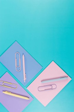 Mavi arka planda pembe, mor ve mavi defterlerin üst görüntüsü. Pembe, sarı ve mavi kalemler, ataçlar, okul, ofis kağıdı. Düz yat, boşluğu kopyala.