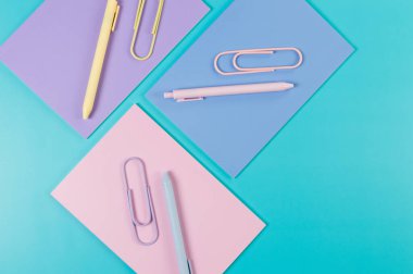 Mavi arka planda pembe, mor ve mavi defterlerin üst görüntüsü. Pembe, sarı ve mavi kalemler, ataçlar, okul, ofis kağıdı. Düz yat, boşluğu kopyala.