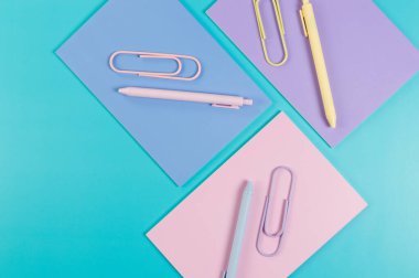 Mavi arka planda pembe, mor ve mavi defterlerin üst görüntüsü. Pembe, sarı ve mavi kalemler, ataçlar, okul, ofis kağıdı. Düz yat, boşluğu kopyala.