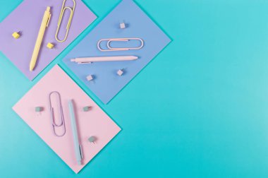 Mavi arka planda pembe, mor ve mavi defterlerin üst görüntüsü. Renkli kalemler, ataçlar, raptiyeler, okul, ofis kağıdı. Düz yat, boşluğu kopyala.