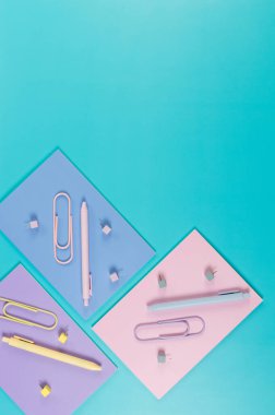 Mavi arka planda pembe, mor ve mavi defterlerin üst görüntüsü. Renkli kalemler, ataçlar, raptiyeler, okul, ofis kağıdı. Düz yat, boşluğu kopyala.