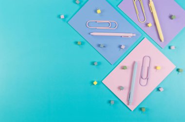 Mavi arka planda pembe, mor ve mavi defterlerin üst görüntüsü. Renkli kalemler, ataçlar, raptiyeler, okul, ofis kağıdı. Düz yat, boşluğu kopyala.