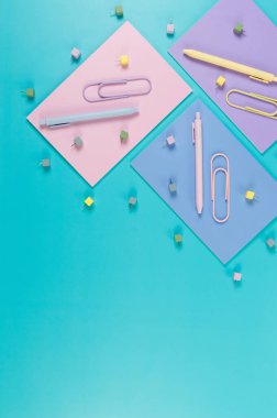 Mavi arka planda pembe, mor ve mavi defterlerin üst görüntüsü. Renkli kalemler, ataçlar, raptiyeler, okul, ofis kağıdı. Düz yat, boşluğu kopyala.