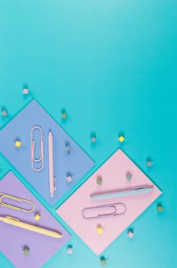 Mavi arka planda pembe, mor ve mavi defterlerin üst görüntüsü. Renkli kalemler, ataçlar, raptiyeler, okul, ofis kağıdı. Düz yat, boşluğu kopyala.