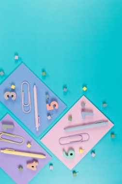 Mavi arka planda pembe, mor ve mavi defterlerin üst görüntüsü. Renkli kalemler, ataçlar, numaralar ve iğneler. Okul, ofis duvar kağıdı. Düz yat, boşluğu kopyala.