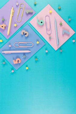 Mavi arka planda pembe, mor ve mavi defterlerin üst görüntüsü. Renkli kalemler, ataçlar, numaralar ve iğneler. Okul, ofis duvar kağıdı. Düz yat, boşluğu kopyala.