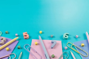 Mavi arka planda pembe, mor ve mavi defterlerin üst görüntüsü. Renkli kalemler, kalemler, ataçlar, sayılar, şekiller ve iğneler. Okul, ofis duvar kağıdı. Düz yat, boşluğu kopyala.