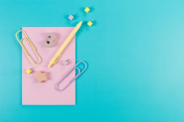 Mavi arkaplanda pembe defterin üst görüntüsü. Ataç, kalem, numara, şekil ve iğne. Okul, ofis duvar kağıdı. Düz yat, boşluğu kopyala.