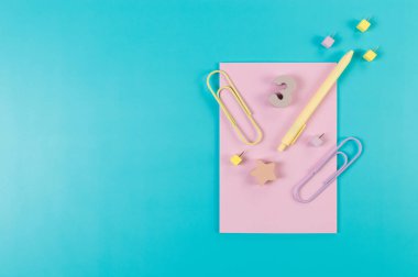 Mavi arkaplanda pembe defterin üst görüntüsü. Ataç, kalem, numara, şekil ve iğne. Okul, ofis duvar kağıdı. Düz yat, boşluğu kopyala.