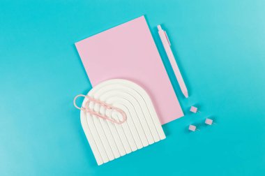 Pembe defter, pembe kalem, ataç, raptiye, mavi arka planda beyaz kemer tepsisi. Okul, ofis duvar kağıdı. Düz yat, boşluğu kopyala.