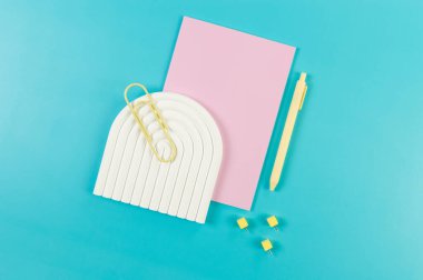 Pembe defterin üst görüntüsü, sarı kalem, ataç, raptiyeler, mavi arka planda beyaz kemer tepsisi. Okul, ofis duvar kağıdı. Düz yat, boşluğu kopyala.