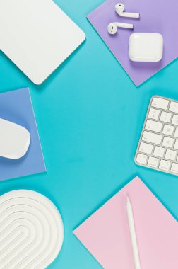 Beyaz klavye, fare, dokunmatik ped, kulaklık kutusu, mavi arka planda kalem. Mor, pembe ve mavi defterler, modern ofis, okul. Beyaz kemer tepsisi, düz konum, kopyalama alanı.