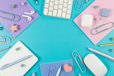 Beyaz klavye, fare, dokunmatik ped, kulaklık kutusu, mavi arka planda kalem. Mor, pembe ve mavi defterler, kalemler, kalemler, ataçlar, iğneler. Modern ofis, okul. Düz yat, boşluğu kopyala.