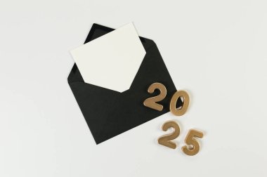 2025 mutlu yıllar. Altın numaraların üst görüntüsü, siyah zarf, beyaz arka planda beyaz kart. Uzayı kopyala, düz yat.