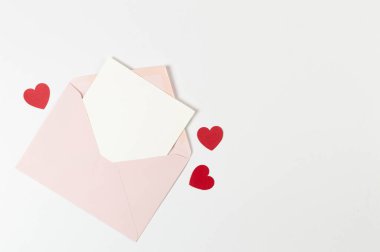 Pembe zarfın üst görüntüsü, beyaz arka planda beyaz kart. Sevgililer günü, kırmızı kalpler, aşk. Düz yatay, kopyala boşluk.
