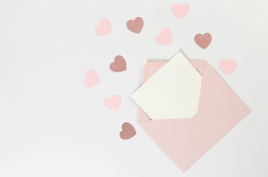 Pembe zarfın üst görüntüsü, beyaz arka planda beyaz kart. Sevgililer günü, pembe kalpler, pembe pırıltılı kalp, aşk. Düz yatay, kopyala boşluk.