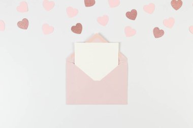 Pembe zarfın üst görüntüsü, beyaz arka planda beyaz kart. Sevgililer günü, pembe kalpler, pembe pırıltılı kalp, aşk. Düz yatay, kopyala boşluk.