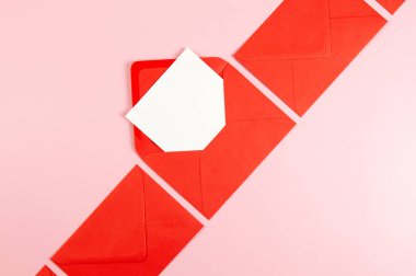 Kırmızı zarfların üst görüntüsü, pembe arka planda beyaz kart. Yat yere. Boşluğu kopyala.