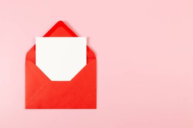 Kırmızı zarfın üst görüntüsü, pembe arka planda beyaz kart. Yat yere. Boşluğu kopyala.