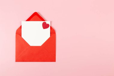 Kırmızı zarfın üst görüntüsü, pembe arka planda beyaz kart. Sevgililer günü, kırmızı kalp, aşk. Düz yatay, kopyala boşluk.