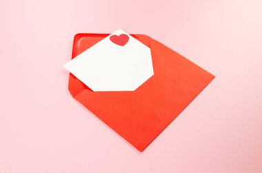 Kırmızı zarfın üst görüntüsü, pembe arka planda beyaz kart. Sevgililer günü, kırmızı kalp, aşk. Düz yatay, kopyala boşluk.