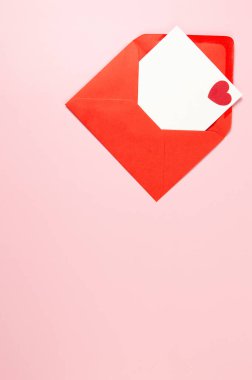 Kırmızı zarfın üst görüntüsü, pembe arka planda beyaz kart. Sevgililer günü, kırmızı kalp, aşk. Düz yatay, kopyala boşluk.