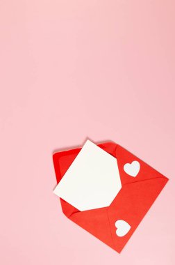 Kırmızı zarfın üst görüntüsü, pembe arka planda beyaz kart. Sevgililer günü, beyaz kalpler, aşk. Düz yatay, kopyala boşluk.